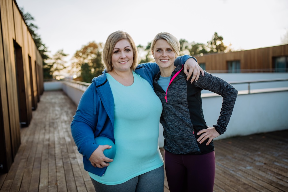 Eine Frau umarmt lächelnd ihren Personal Trainer im Freien nach dem Training
